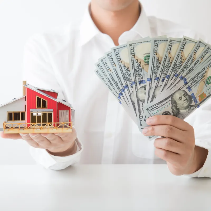Person holding a model house in one hand and cash in the other