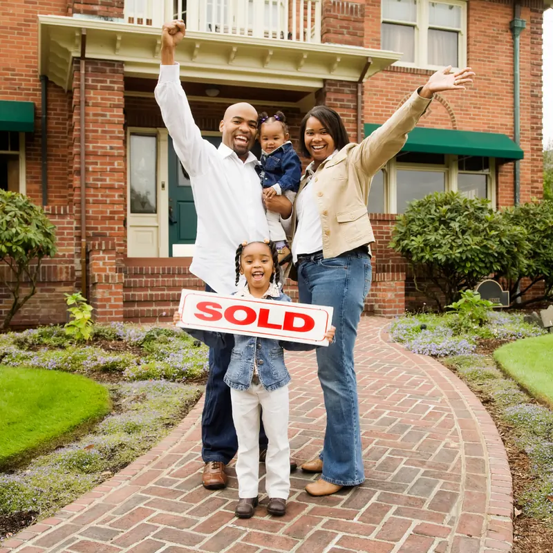 Happy family holding a sold sign in front of their house