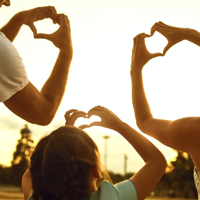 Family making heart shapes with their hands at sunset